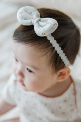 Close-up of baby wearing Avauma Rose Garden Petite Garden Headband with delicate pink rose floral bow